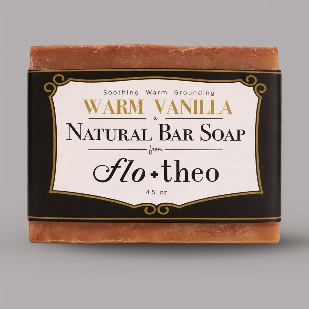Bar of warm vanilla natural soap with 'flo + theo' branding on a gray background