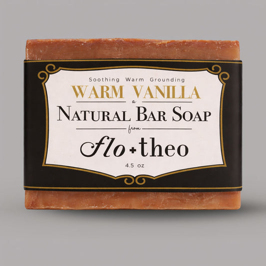Bar of warm vanilla natural soap with 'flo + theo' branding on a gray background